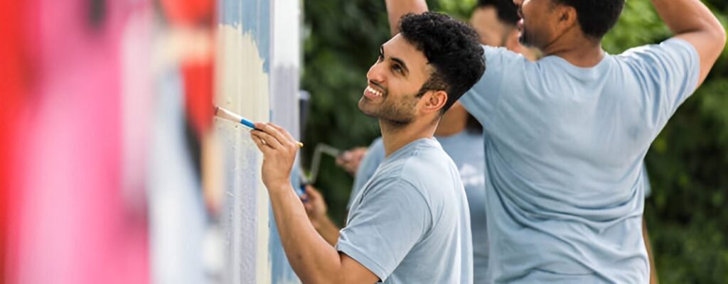 Hombres colaborando en la restauración de una barda mediante la aplicación de pintura